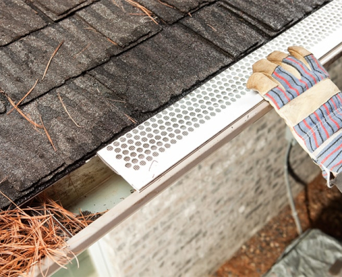 A person installing a gutter using a tool, demonstrating home maintenance and improvement skills