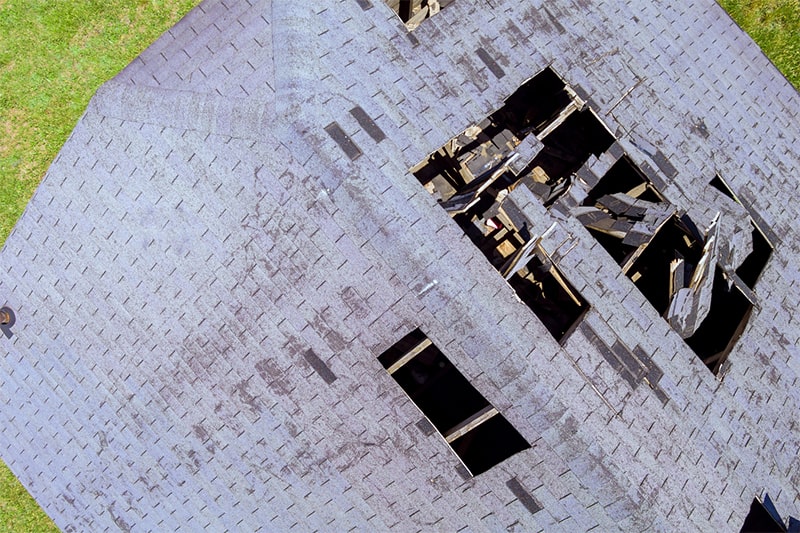 Aerial view of a damaged roof, showcasing visible structural issues and debris scattered across the surface.