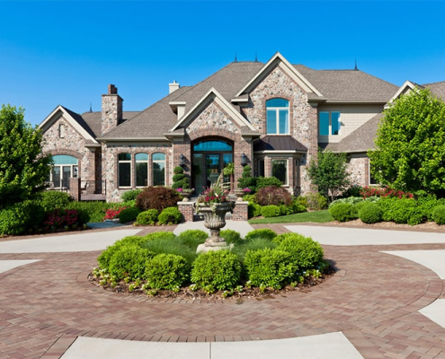 A spacious brick driveway leads to a grand home, featuring an elegant fountain at its entrance